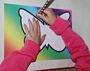 Using the stencil to trace the butterfly shape onto the rainbow paper